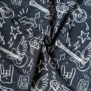 May include: A black fabric featuring a white line-art pattern of electric guitars with wings, skulls, stars, lightning bolts, musical notes, speakers, and hand gestures. The background has a subtle grey speckled texture throughout the material.