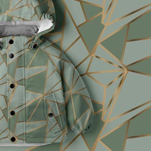 May include: A hooded jacket featuring a sage green base color with a geometric pattern of intersecting gold lines. The jacket includes a front placket with black snap buttons, a hood, and two front pockets with matching snap button closures.