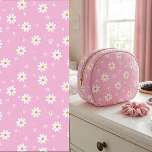 May include: A round, pink cosmetic bag featuring a repeating white daisy pattern with yellow centers and a gold-toned zipper closure. Beside the bag sits a matching pink fabric scrunchie, both displaying the same floral print design.