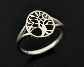 May include: A silver ring featuring a tree of life design. The ring has a polished finish and a detailed cutout of a tree within an oval shape. The band is split on either side of the tree design.