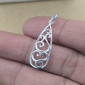 Op de afbeelding: Zilveren hanger met een druppelvorm en een open filigraan ontwerp. De hanger heeft wervelende, scroll-achtige patronen in de druppelomtrek. De beugel is een kleine lus aan de bovenkant voor een ketting.