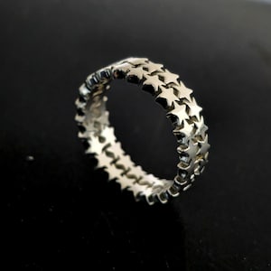 Könnte beinhalten: Ein silberner Ring mit einem sich wiederholenden Sternmuster. Der Ring besteht aus einem glänzenden, metallischen Material mit einem Band aus Sternen, das den gesamten Umfang umschließt. Die Sterne sind gleichmäßig verteilt und bilden ein durchgehendes Muster.