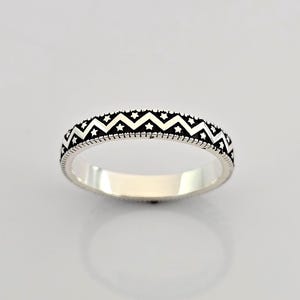 May include: A silver ring featuring a repeating pattern of zigzags and stars. The ring has a polished finish and a detailed design around the band. The ring is a size O.