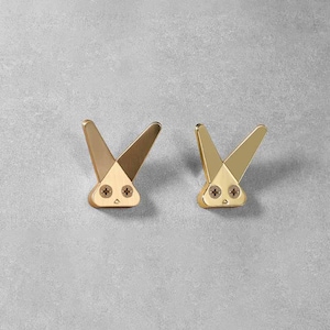 May include: Two gold bunny-shaped hooks with black screw heads. The hooks are mounted on a gray wall.