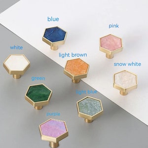 May include: Assortment of eight hexagonal cabinet knobs with a gold metal base and a variety of colored marble-like inlays. The colors include white, snow white, light brown, pink, blue, light blue, green, and purple.