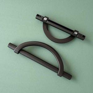 May include: Two black metal cabinet pulls with a half-circle design. One pull is a straight bar with a half-circle cutout, and the other is a curved bar with a half-circle cutout.