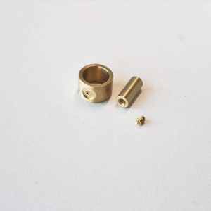May include: A set of three brass hardware components: a cylindrical ring with a side hole, a threaded rod, and a small screw. The items are arranged on a white surface, showcasing their metallic sheen.