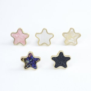 Può includere: Cinque pomelli per mobili a forma di stella con finitura dorata. I pomelli sono realizzati in diversi materiali, tra cui rosa, bianco, blu e nero.