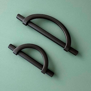 Può includere: Due maniglie per armadi in metallo nero con un design semicircolare. Le maniglie sono di dimensioni diverse.