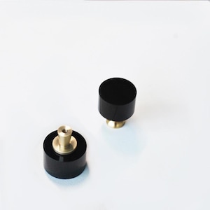 Può includere: Due pomelli rotondi neri per armadio con base in ottone. I pomelli sono realizzati in un materiale liscio e lucido.