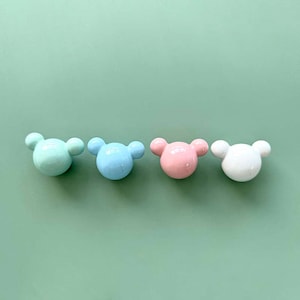 Puede incluir: Cuatro pomos de cerámica con forma de cabeza de oso. Los pomos son de color azul claro, rosa, blanco y verde.