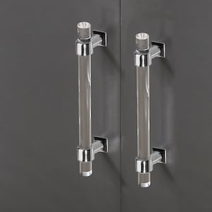 Könnte beinhalten: Zwei klare Acryl-Schrankgriffe mit verchromten Akzenten. Die Griffe sind an einer grauen Oberfläche montiert.