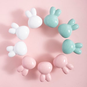 May include: A set of nine ceramic drawer pulls in the shape of bunnies. The pulls are in three colors: white, light pink, and light green.