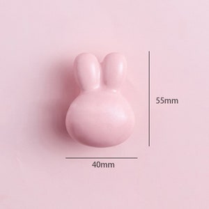 May include: A pink ceramic bunny-shaped drawer pull measuring 40mm wide and 55mm tall.