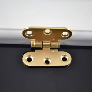 Könnte beinhalten: Ein goldfarbenes Metallgelenk mit vier Löchern auf jeder Seite. Das Gelenk ist geschlossen und die beiden Seiten liegen bündig.