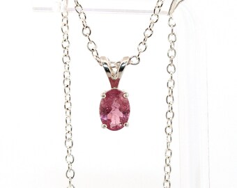May include: A silver necklace featuring a pendant with an oval, pink gemstone. The pendant is set in a silver bezel and hangs from a delicate silver chain. The gemstone has a soft, pink hue and is the focal point of the necklace.