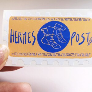 May include: A white sticker with a yellow background and a blue circle containing a stylized image of winged sandals. The text "HERMES POST" is written in blue on the sticker.