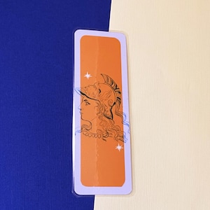 Op de afbeelding: Oranje bladwijzer met een zwart-witte illustratie van een vrouw met een helm en een stervormig ontwerp.