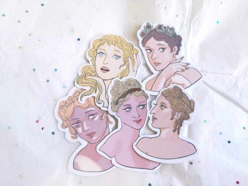 Puede incluir: Un conjunto de pegatinas troqueladas con ilustraciones de mujeres con peinados y vestimentas cl&aacute;sicas. Las pegatinas muestran diversos tonos de piel y colores de cabello, algunas adornadas con coronas de laurel. La obra de arte tiene una paleta de colores pastel suaves.
