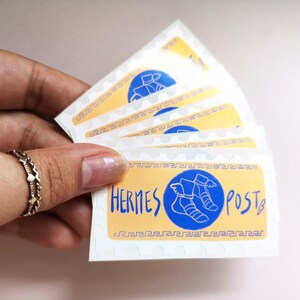 May include: A set of five stickers featuring a yellow background with a blue circle containing a winged sandal. The text "HERMES POST" is written in blue lettering.