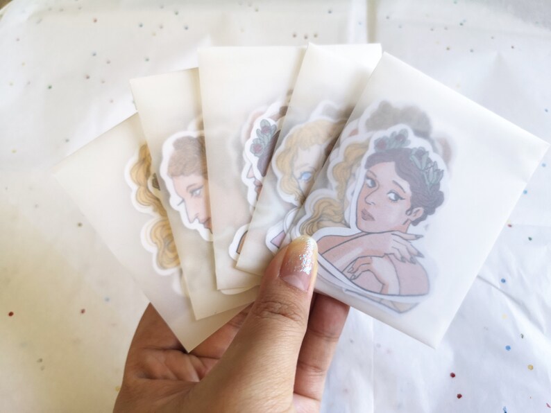 Puede incluir: Una colecci&oacute;n de pegatinas con ilustraciones de mujeres en varias poses, cada una en un paquete transparente. Las pegatinas muestran ilustraciones detalladas con paletas de colores suaves y l&iacute;neas delicadas. Las pegatinas se sostienen en una mano.