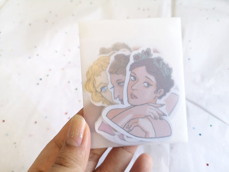 Puede incluir: Un conjunto de pegatinas con ilustraciones de mujeres con coronas de flores y retratos cl&aacute;sicos. Las pegatinas est&aacute;n en un paquete transl&uacute;cido, sostenido por una mano. Las ilustraciones tienen una paleta de colores pastel.