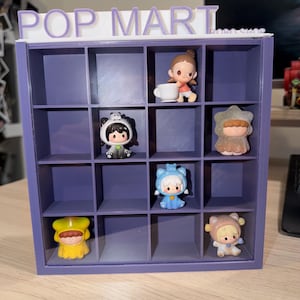 May include: A purple 16-compartment display shelf with the text POP MART on top. Inside the grid are six small collectible figurines: one holding a white cup, one in a panda suit, one in a star costume, one in a blue cat suit, one in a yellow hood, and one in a bear suit.