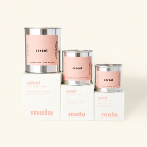 K&ouml;nnte beinhalten: Drei silberne Metallkerzenbeh&auml;lter mit rosa Etiketten, auf denen "cereal" und "mala" steht. Die Kerzen sind mit Kokosnuss und Soja parf&uuml;miert.