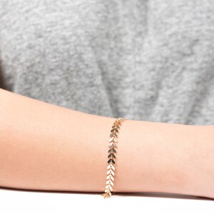 Op de afbeelding: Een gouden armband met een ketting van kleine pijlvormige schakels.