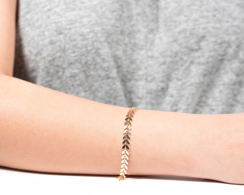 Op de afbeelding: Een gouden armband met een ketting van kleine pijlvormige schakels.