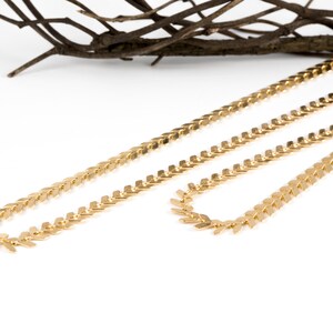 Op de afbeelding: Twee gouden kettingen met een chevron-patroon. De kettingen zijn op elkaar gelegd.