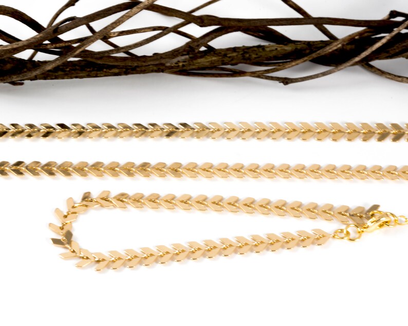Op de afbeelding: Twee gouden kettinghalskettingen met een chevron-patroon. De kortere ketting is een armband.