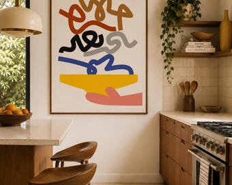 May include: A framed abstract art print with a brown wooden frame. The artwork features colourful, squiggly lines in shades of brown, red, black, grey, and blue, above a yellow shape and a pink hand. The print hangs in a modern kitchen setting.