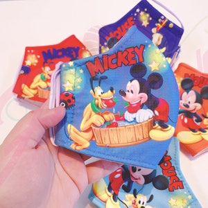 K&ouml;nnte beinhalten: Ein Set aus vier blauen, roten und orangefarbenen Stoffmasken mit Mickey Mouse und Pluto. Die Masken haben verstellbare Ohrschlaufen und sind mit Sternen und dem Schriftzug "Mickey Mouse" verziert.