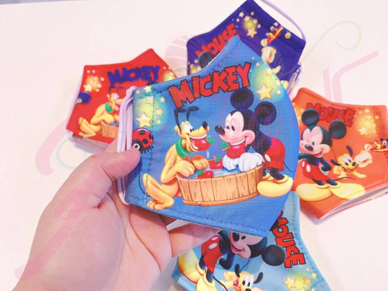K&ouml;nnte beinhalten: Ein Set aus vier blauen, roten und orangefarbenen Stoffmasken mit Mickey Mouse und Pluto. Die Masken haben verstellbare Ohrschlaufen und sind mit Sternen und dem Schriftzug "Mickey Mouse" verziert.
