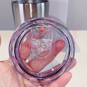 Puede incluir: Una tapa de pl&aacute;stico transparente con un borde morado y un mecanismo de cierre. La tapa est&aacute; dise&ntilde;ada para encajar en un vaso de acero inoxidable.