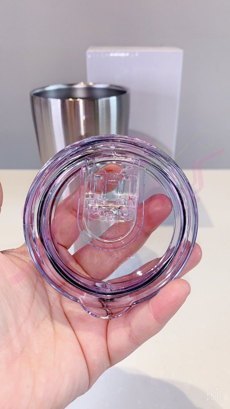 Puede incluir: Una tapa de pl&aacute;stico transparente con un borde morado y un mecanismo de cierre. La tapa est&aacute; dise&ntilde;ada para encajar en un vaso de acero inoxidable.