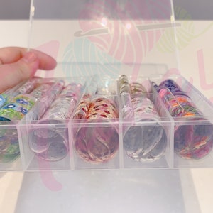 May include: A clear plastic storage box with multiple compartments, each containing a roll of colorful patterned nail art foil.