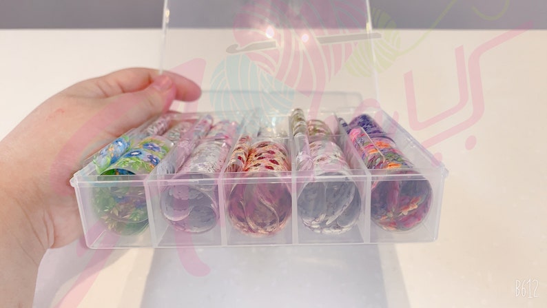 May include: A clear plastic storage box with multiple compartments, each containing a roll of colorful patterned nail art foil.