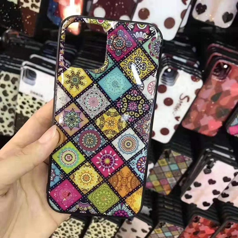 May include: A black phone case with a colorful mandala pattern. The pattern is made up of various shades of pink, blue, yellow, and green. The case has a glossy finish.