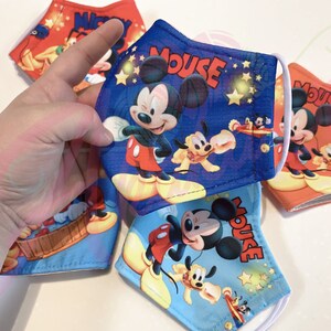 K&ouml;nnte beinhalten: Vier blaue und rote Stoffmasken mit Mickey-Mouse-Motiv. Die Masken zeigen Mickey Mouse, Pluto und ein Flugzeug. Der Text "Mouse" ist auf jeder Maske aufgedruckt.