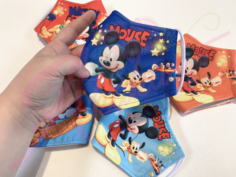 K&ouml;nnte beinhalten: Vier blaue und rote Stoffmasken mit Mickey-Mouse-Motiv. Die Masken zeigen Mickey Mouse, Pluto und ein Flugzeug. Der Text "Mouse" ist auf jeder Maske aufgedruckt.