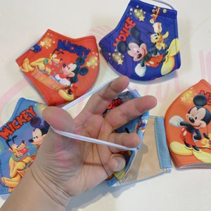K&ouml;nnte beinhalten: Vier farbenfrohe Gesichtsmasken mit Mickey Mouse und Pluto. Die Masken sind aus Stoff und haben elastische Ohrschlaufen. Die Masken sind mit verschiedenen Designs bedruckt, darunter Mickey Mouse, Pluto und Sterne.