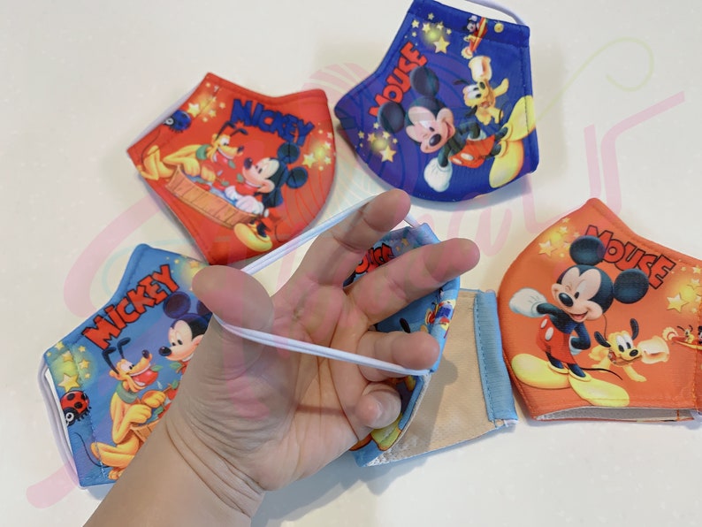 K&ouml;nnte beinhalten: Vier farbenfrohe Gesichtsmasken mit Mickey Mouse und Pluto. Die Masken sind aus Stoff und haben elastische Ohrschlaufen. Die Masken sind mit verschiedenen Designs bedruckt, darunter Mickey Mouse, Pluto und Sterne.