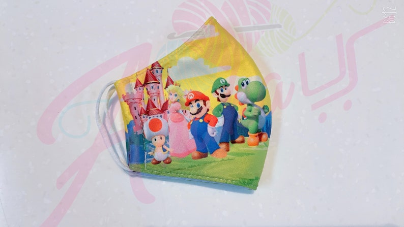May include: A yellow, green, and pink face mask with a cartoon image of Mario, Luigi, Peach, Toad, and Yoshi in front of a pink castle.