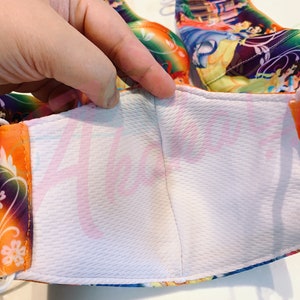 May include: A white face mask with a colourful Disney Princesses print. The mask has a white inner layer and orange elastic straps.