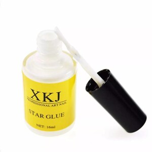 May include: A bottle of Star Glue for professional art nails. The bottle is white with a yellow label that has black text. The black cap is off, revealing a white brush applicator. The bottle contains 16ml of glue.