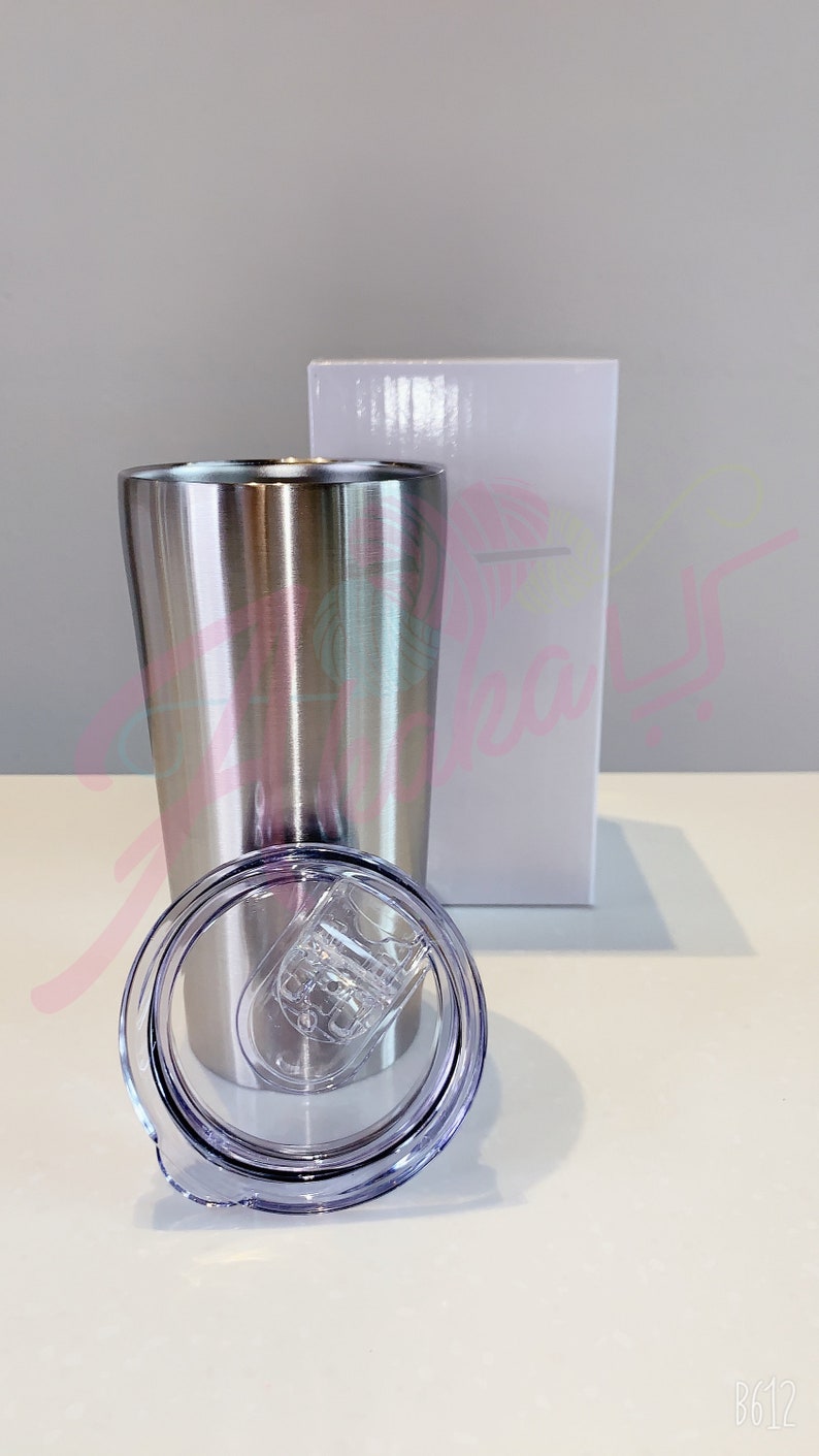 Puede incluir: Un vaso de acero inoxidable con una tapa transparente. El vaso es plateado y tiene un acabado cepillado. La tapa tiene una junta de silicona alrededor del borde.