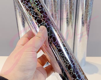 May include: A roll of iridescent silver holographic vinyl with a cracked or textured pattern. The vinyl is rolled up and held in a hand.