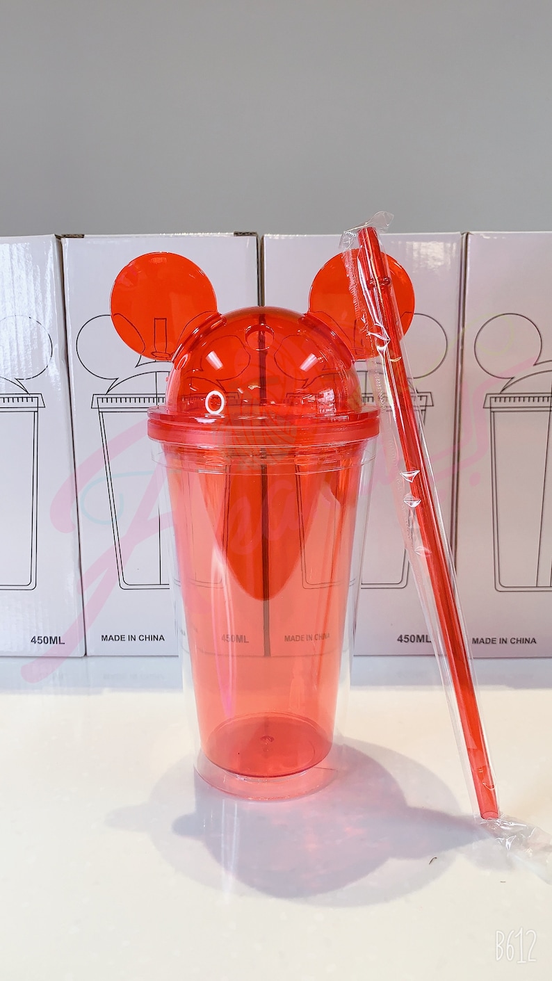 May include: Red plastic tumbler with Mickey Mouse ears and a straw. The tumbler is clear with a red lid and has a 450 ml capacity. The tumbler is made in China.